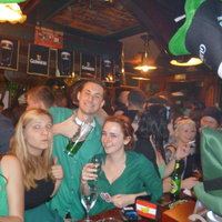 Gäste sitzen an der Theke des Pubs und tragen grüne Oberteile
