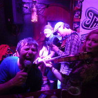 Fünf Musiker stehen im Neonlicht auf der Bühne des Pubs