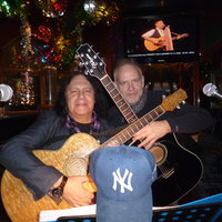 Zwei Gitarristen sitzen nebeneinander hinter zwei Mikrofonen